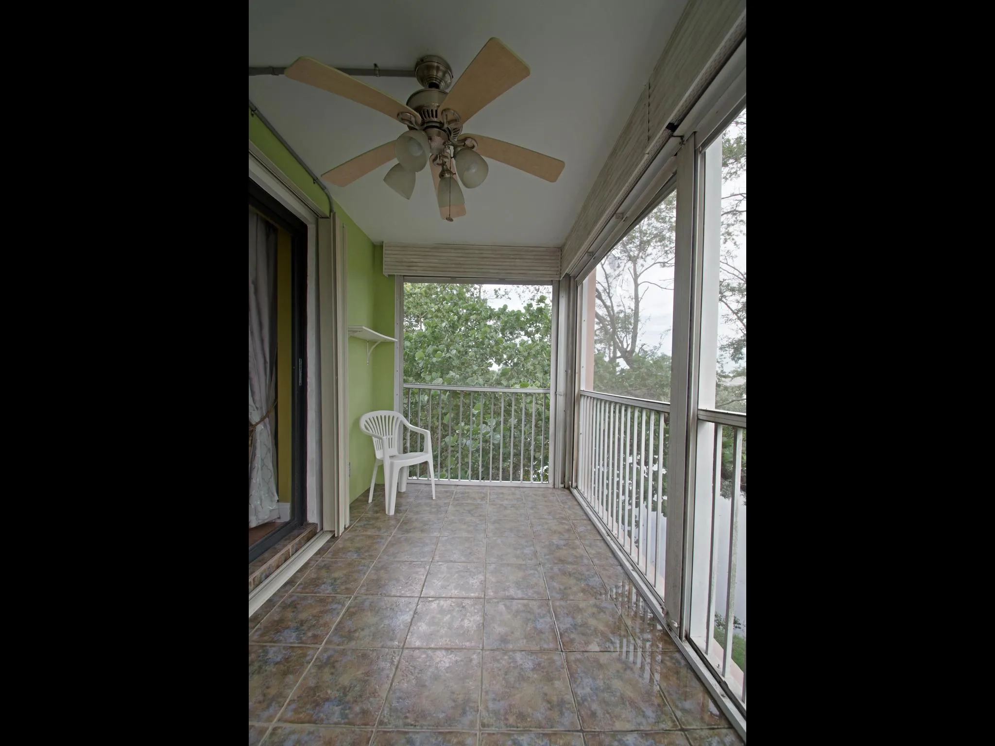 Screened-in balcony featuring a ceiling fan with integrated lighting, tiled flooring, and a white balustrade