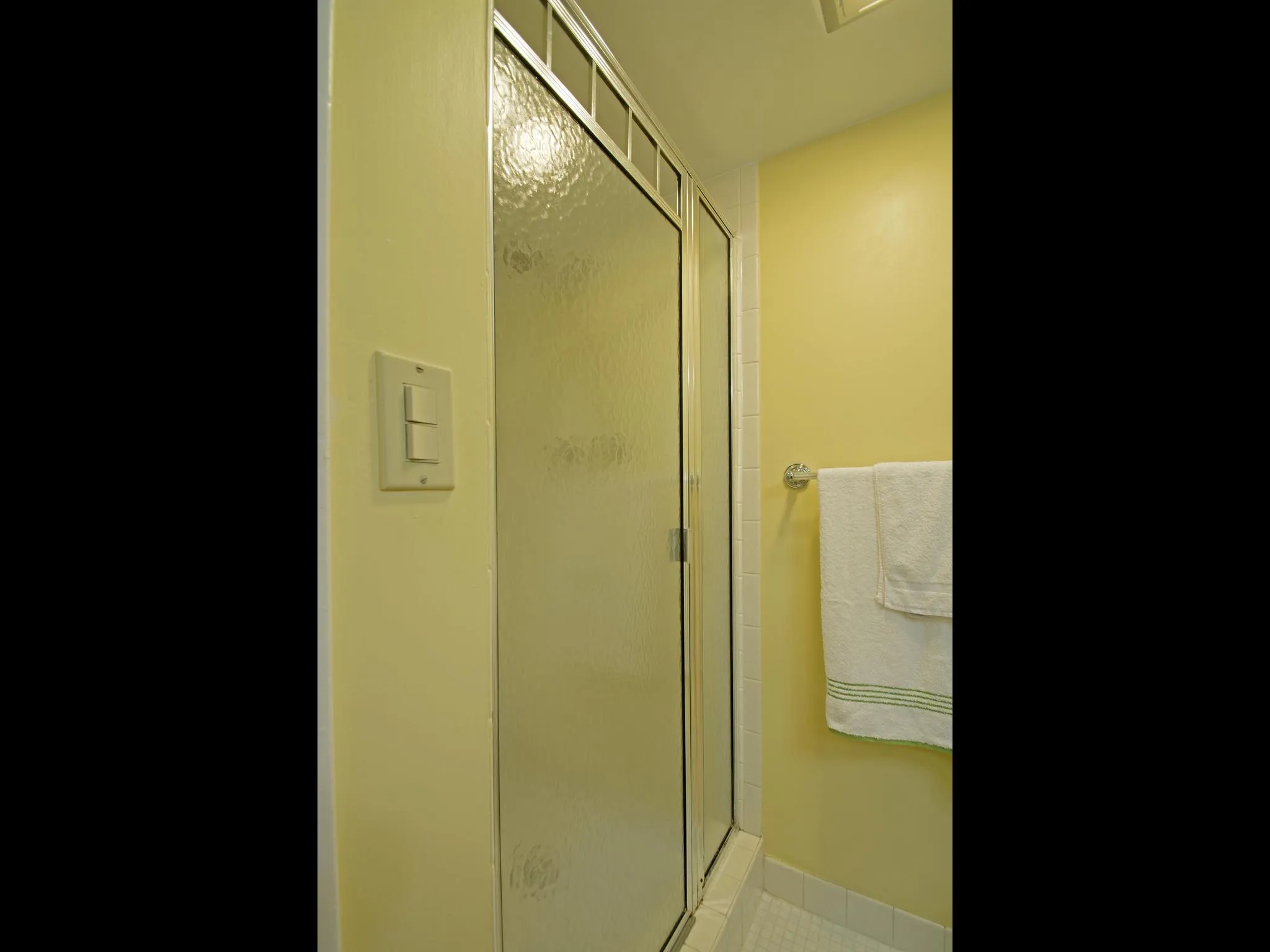 Enclosed shower with textured glass door, metal framing, and white tiled base