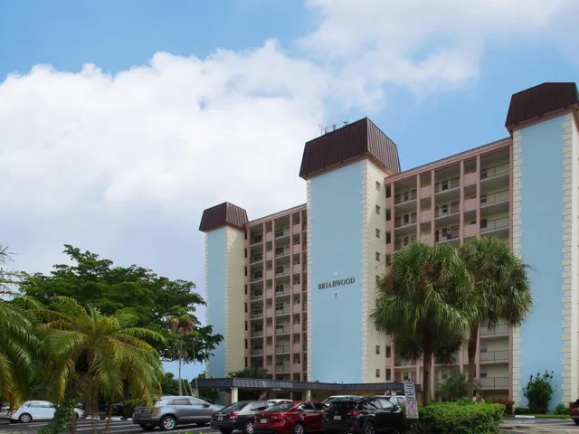 Mid-rise residential building featuring multiple balconies, a covered entryway, and mature palm trees