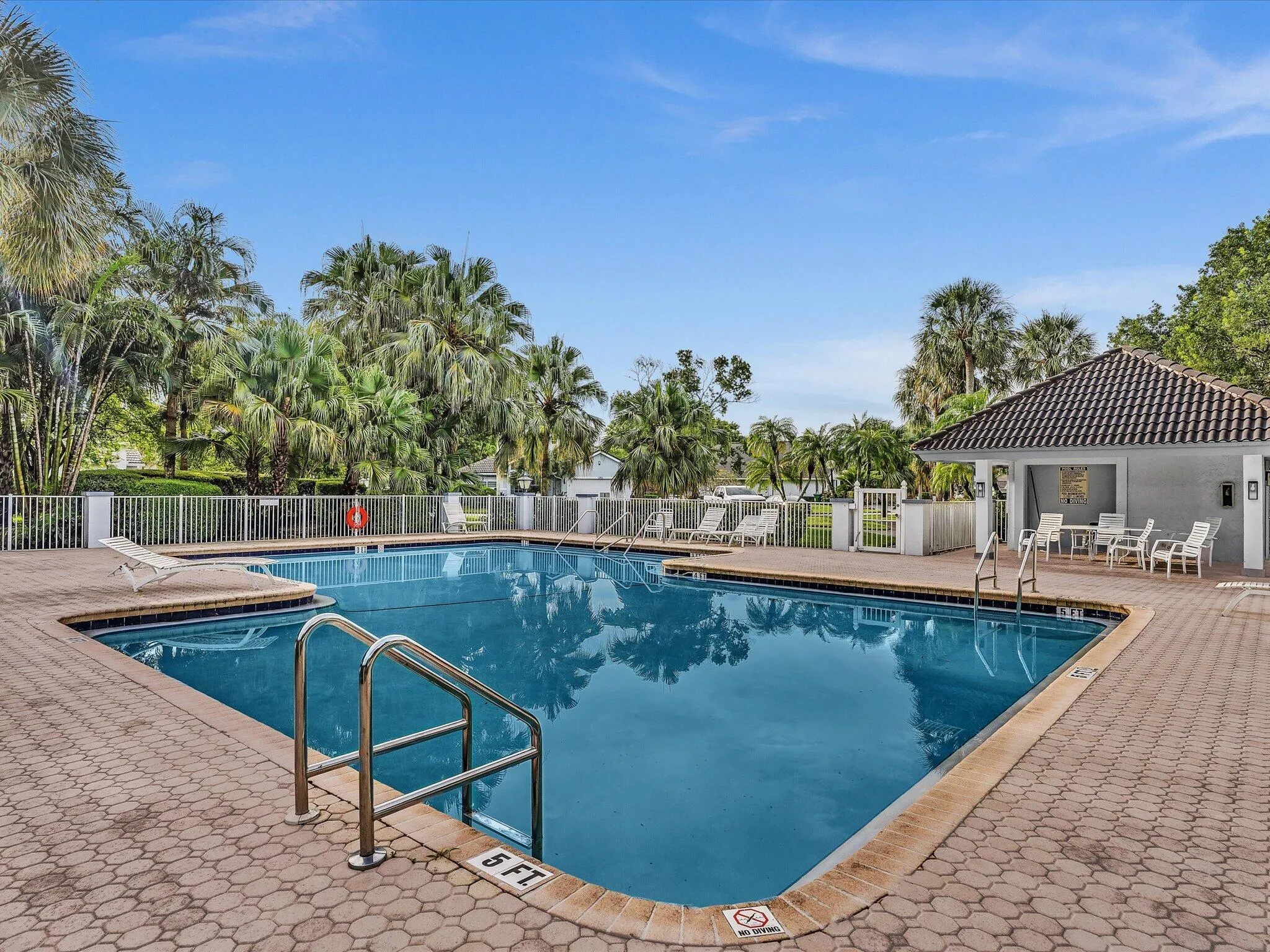 Swimming pool with paver decking, surrounding fence, and tropical landscaping