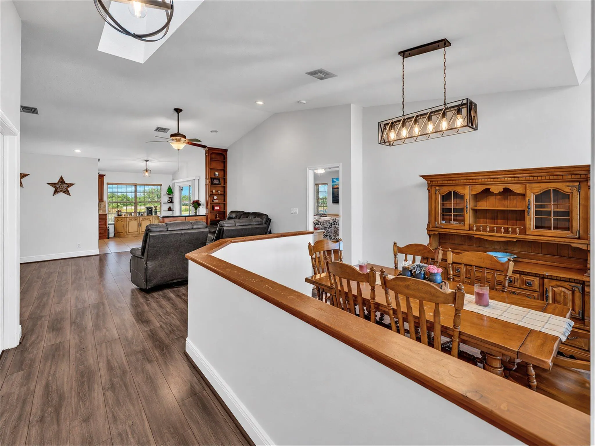 Vaulted ceilings with recessed lighting, wood-finish flooring, a built-in wood-finish shelving unit, a skylight, and an industrial-style chandelier
