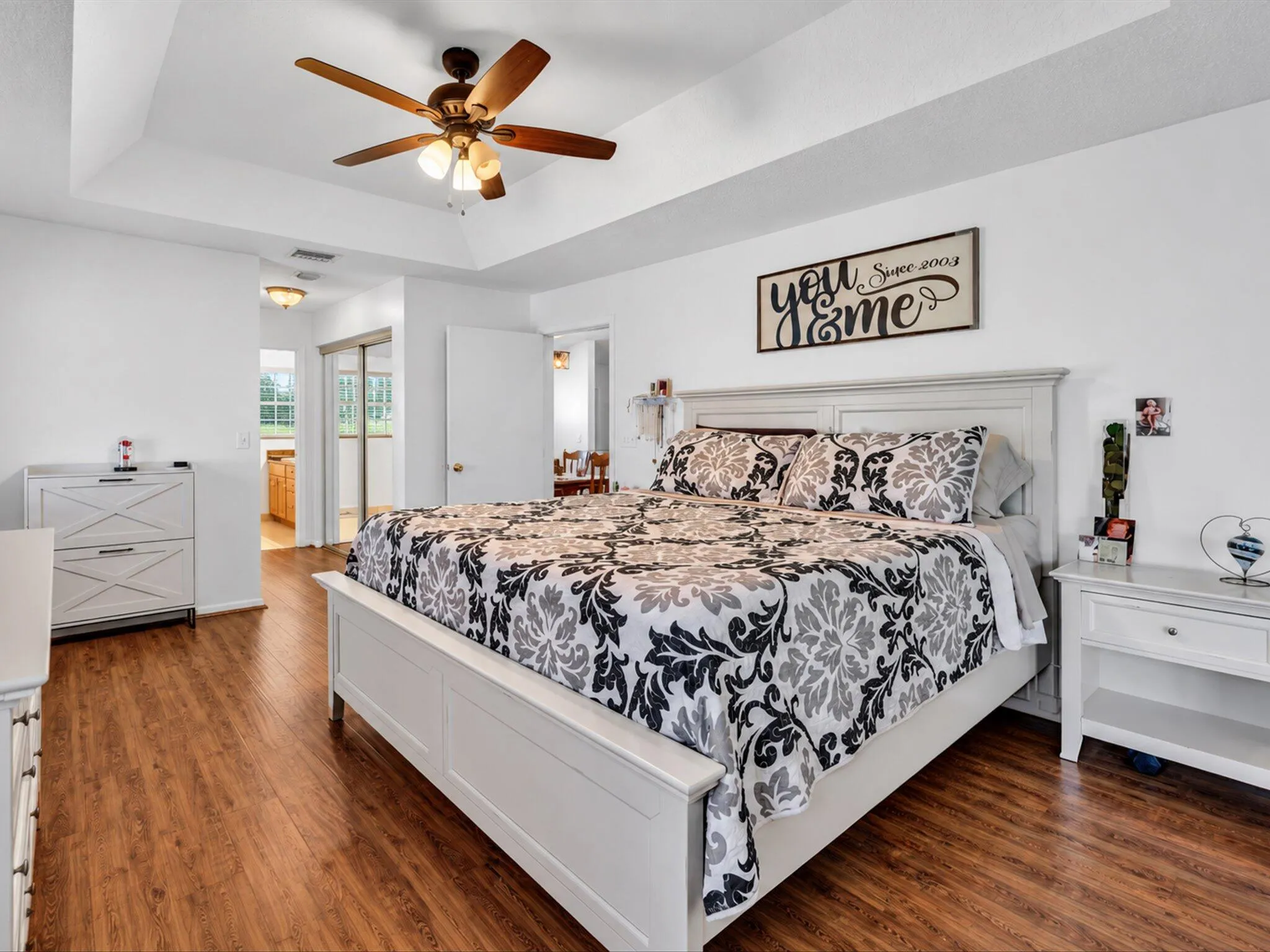 Tray ceiling with a ceiling fan, wood-finish flooring, white walls, and a sliding mirrored closet door