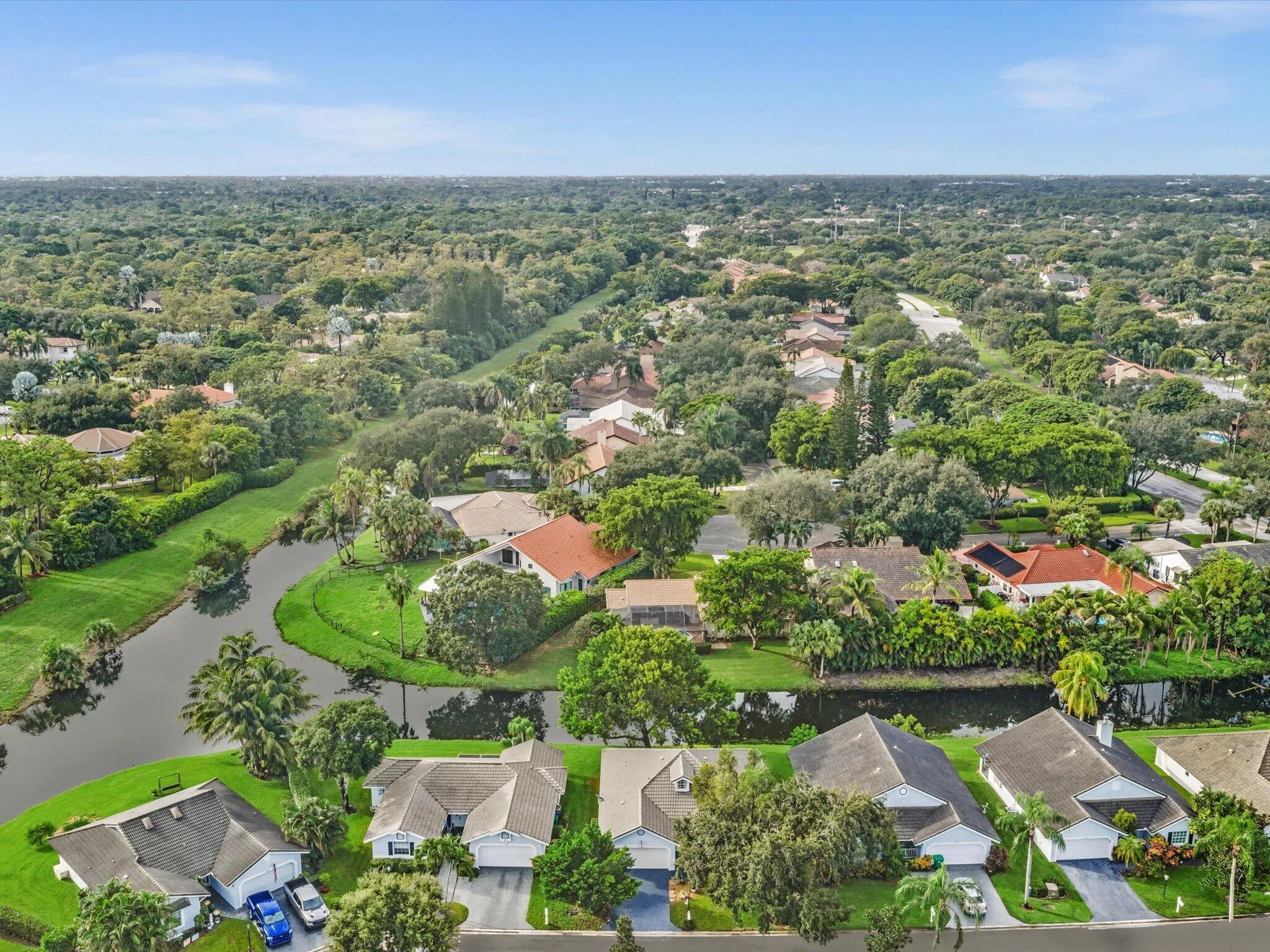 Aerial neighborhood perspective with mature trees, established residential properties, and a prominent waterway