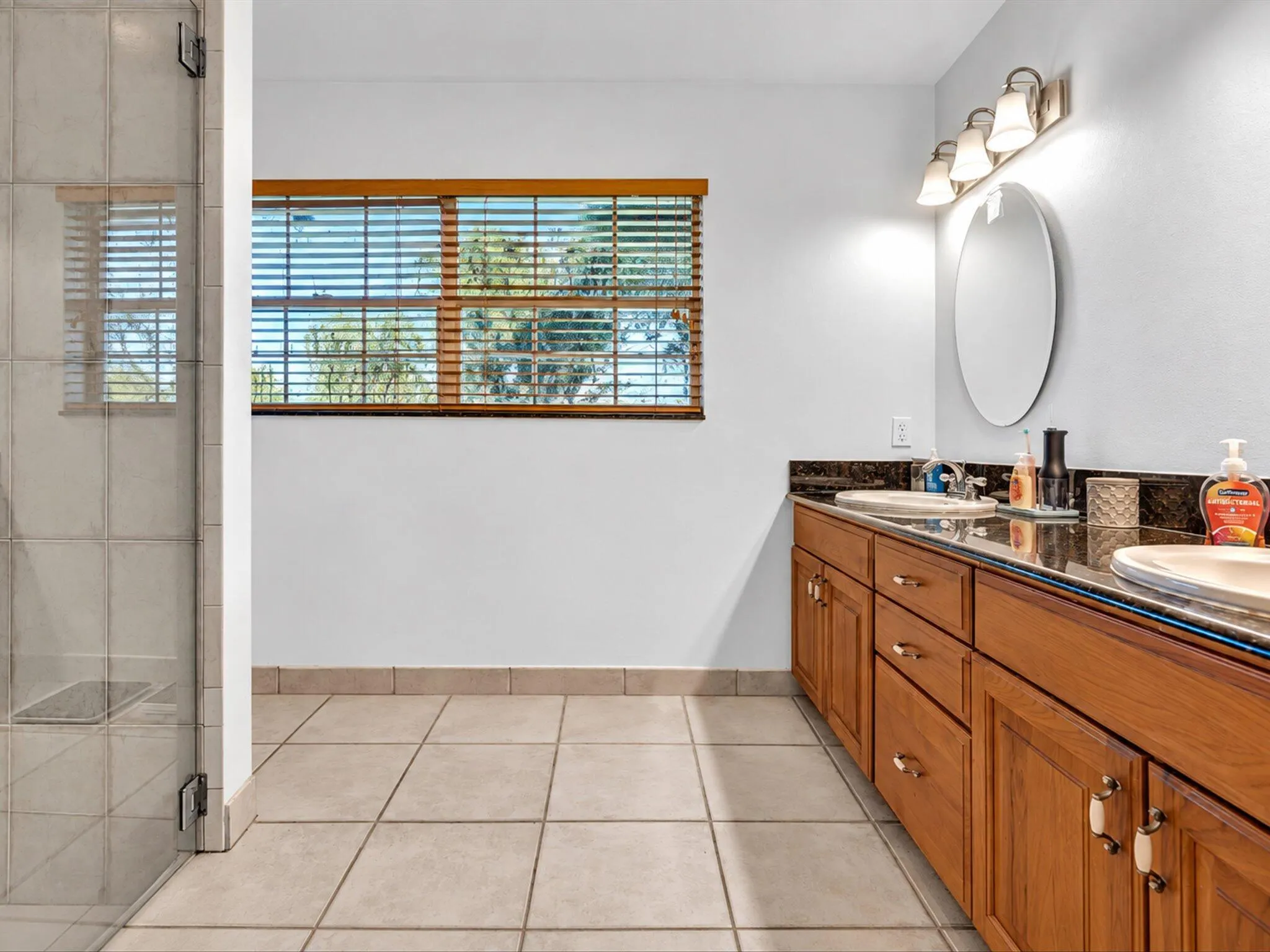 Tiled flooring, wood-finish vanity with dual sinks, stone countertop, and a walk-in shower with glass enclosure
