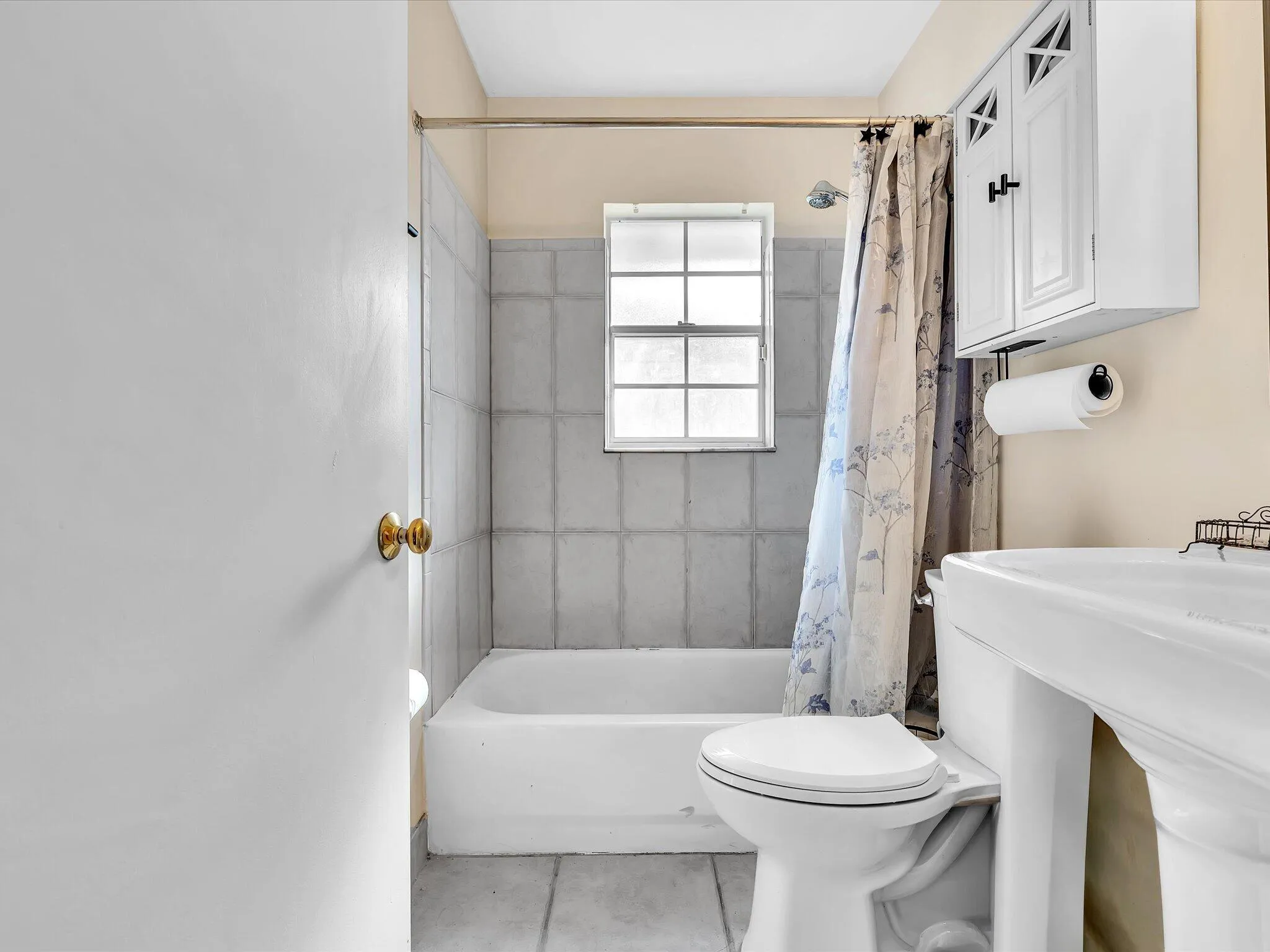White pedestal sink with a white toilet, tiled flooring, and a window for natural light