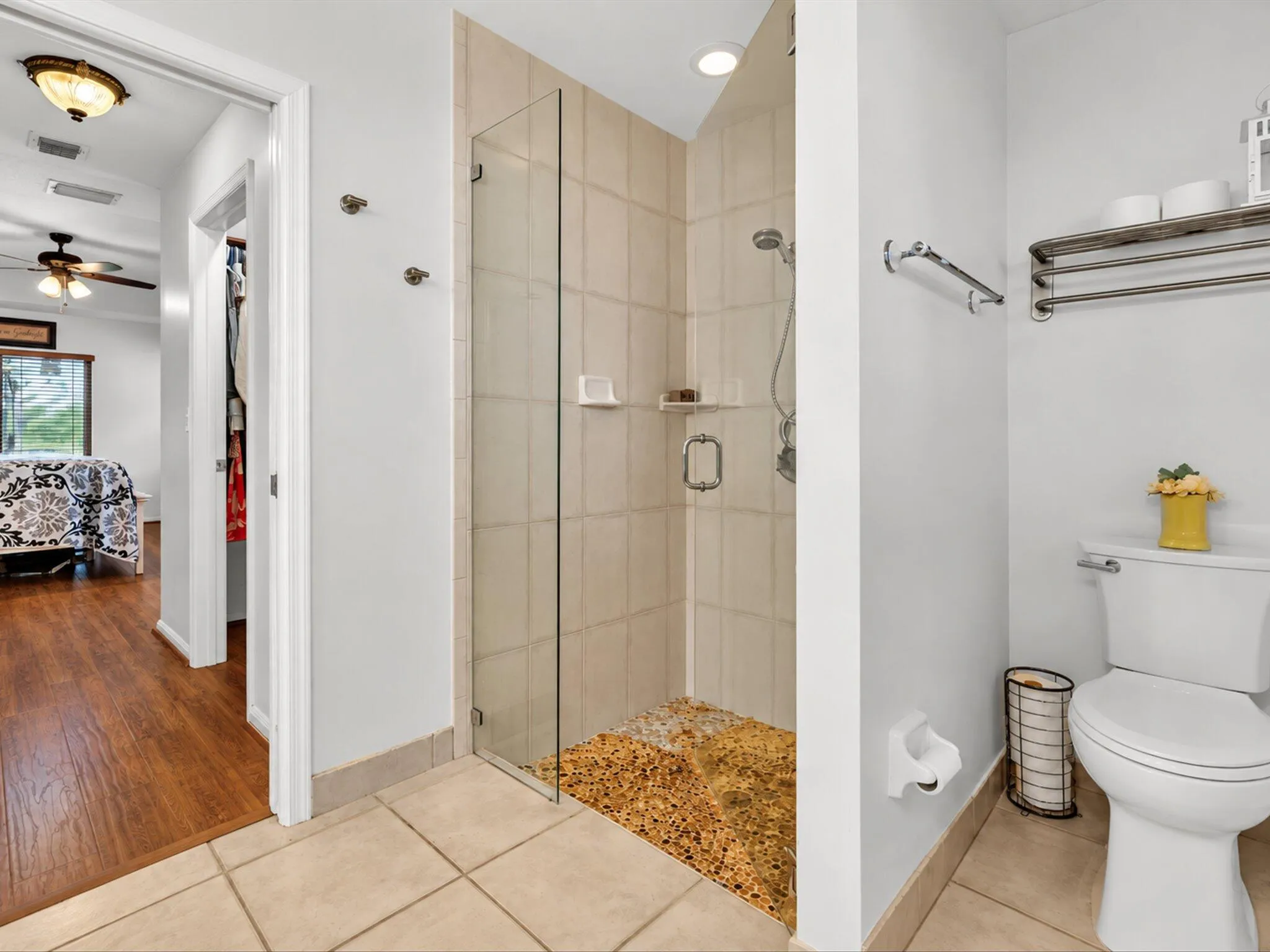 Glass-enclosed shower with pebble-style flooring, tiled walls, and a recessed light