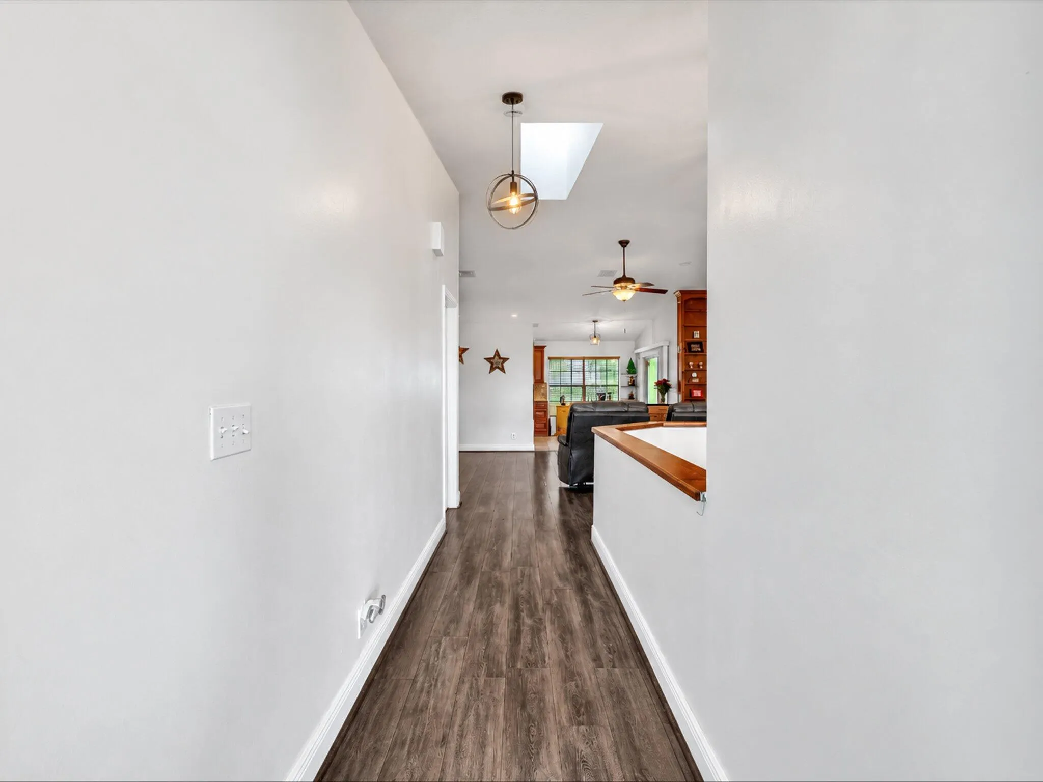 Hallway featuring wood-finish flooring, a skylight, and a contemporary pendant light fixture