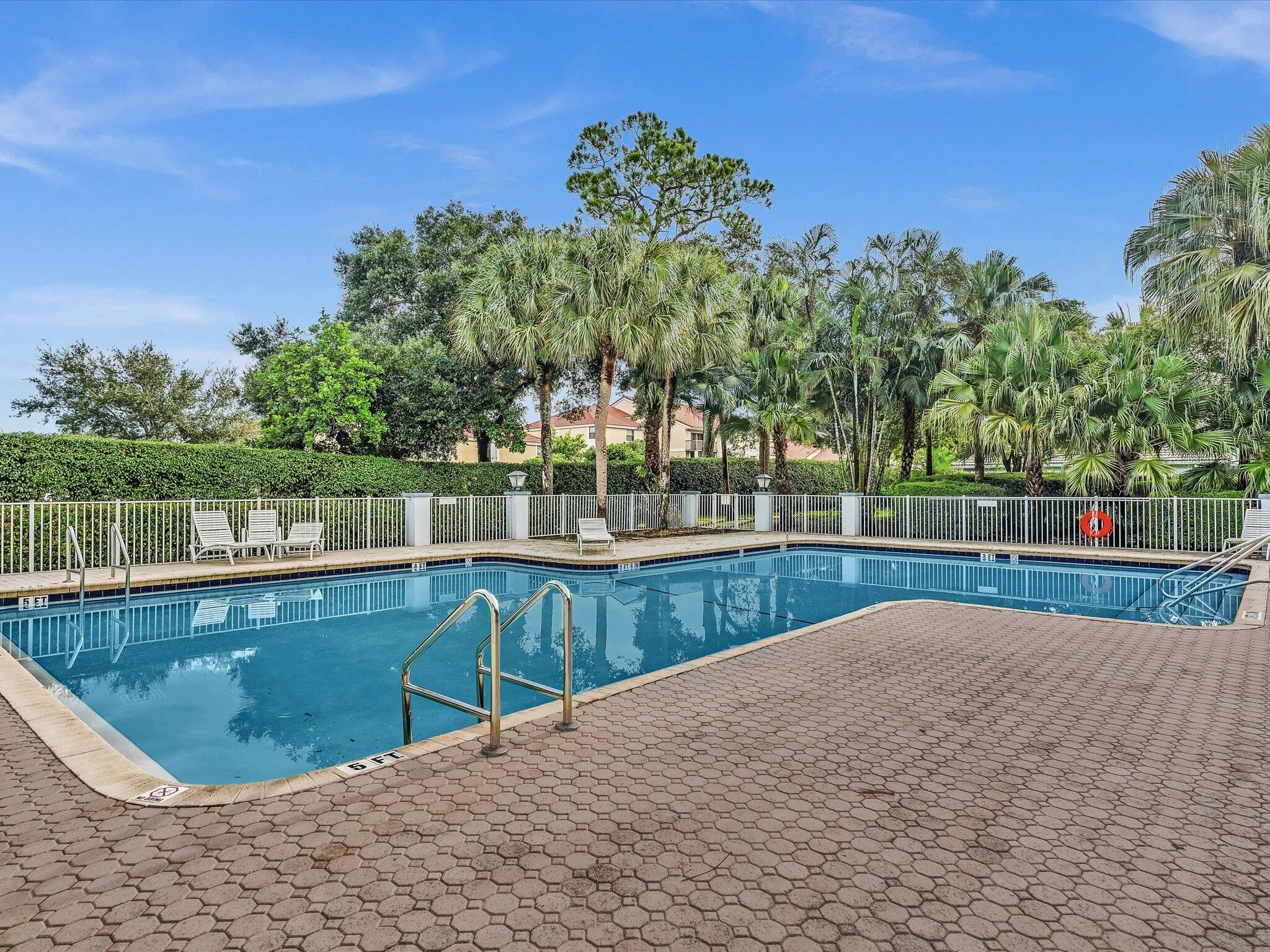Rectangular swimming pool with integrated steps, surrounded by a paver deck, and secured by a white perimeter fence