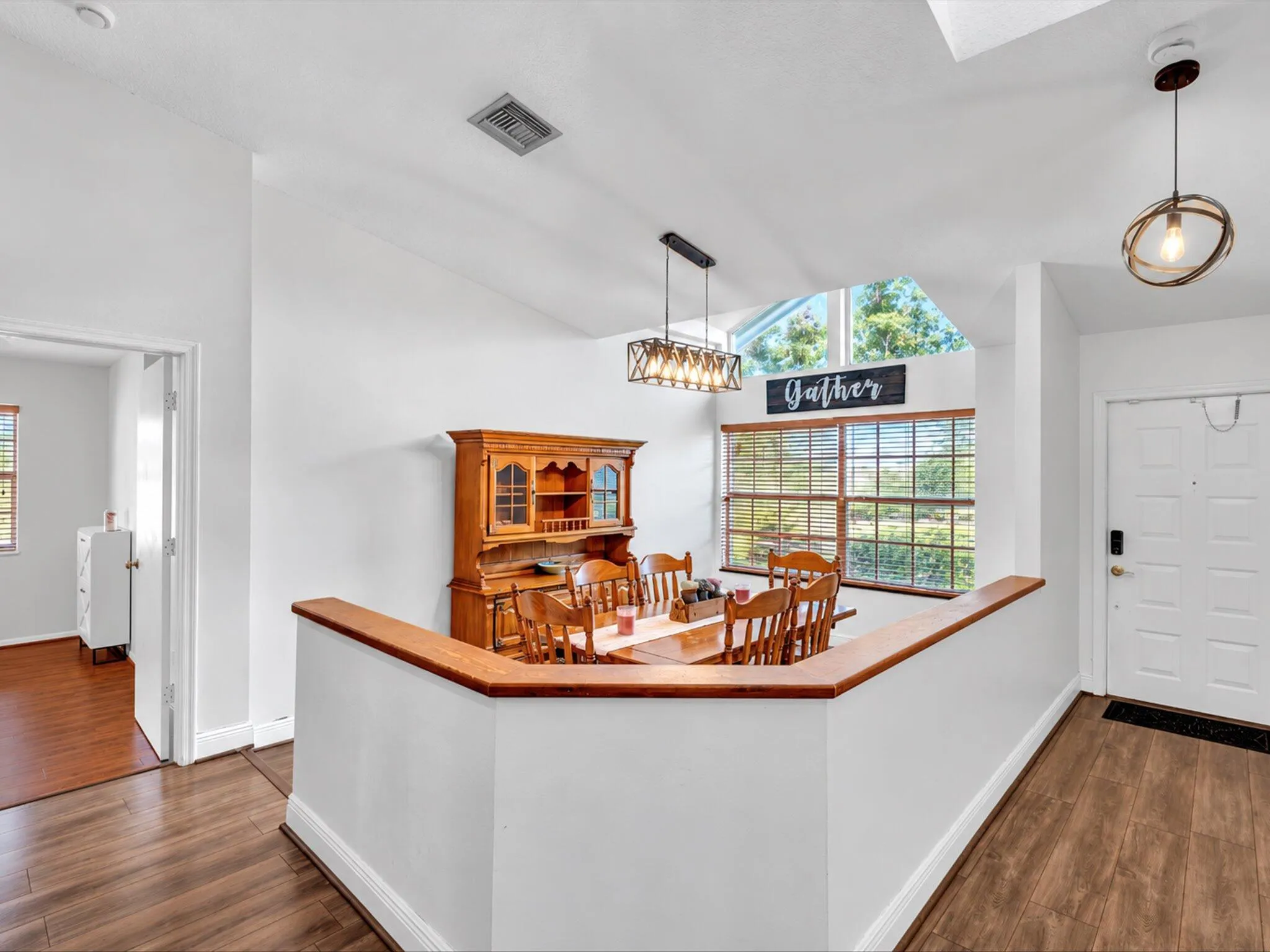 Vaulted ceiling, wood-finish flooring, half-wall with wood-finish cap, large windows, and modern pendant lighting