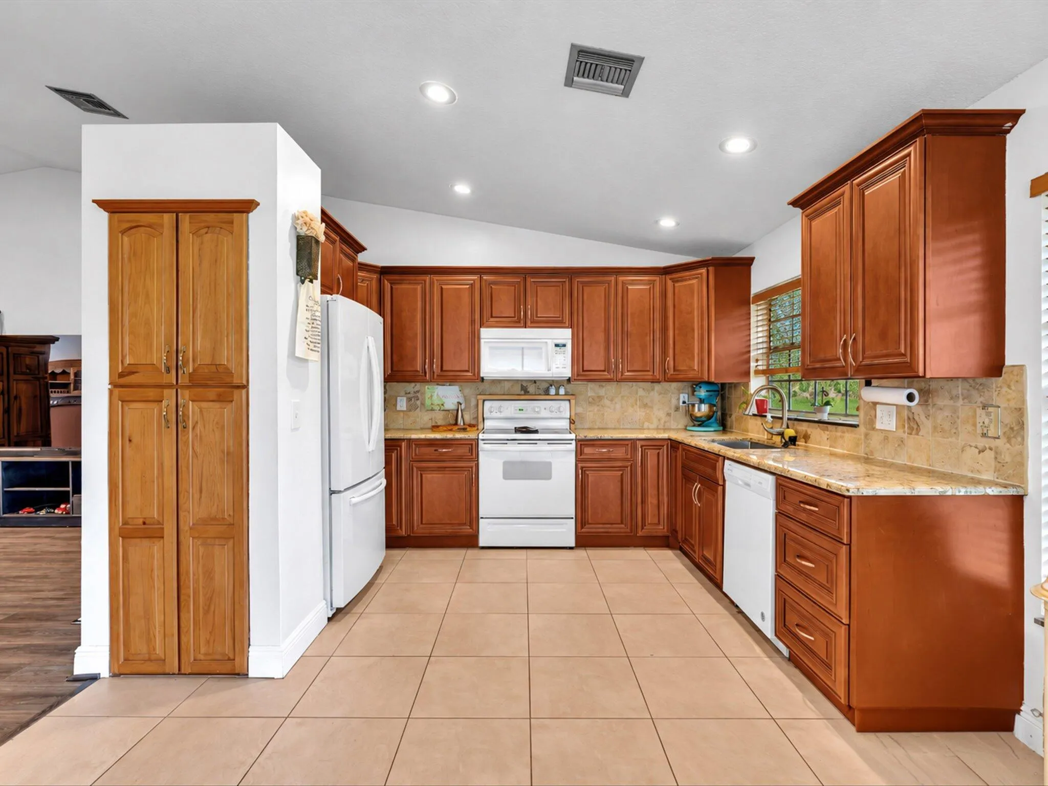 U-shaped kitchen featuring wood cabinetry, white appliances, recessed lighting, and tile flooring