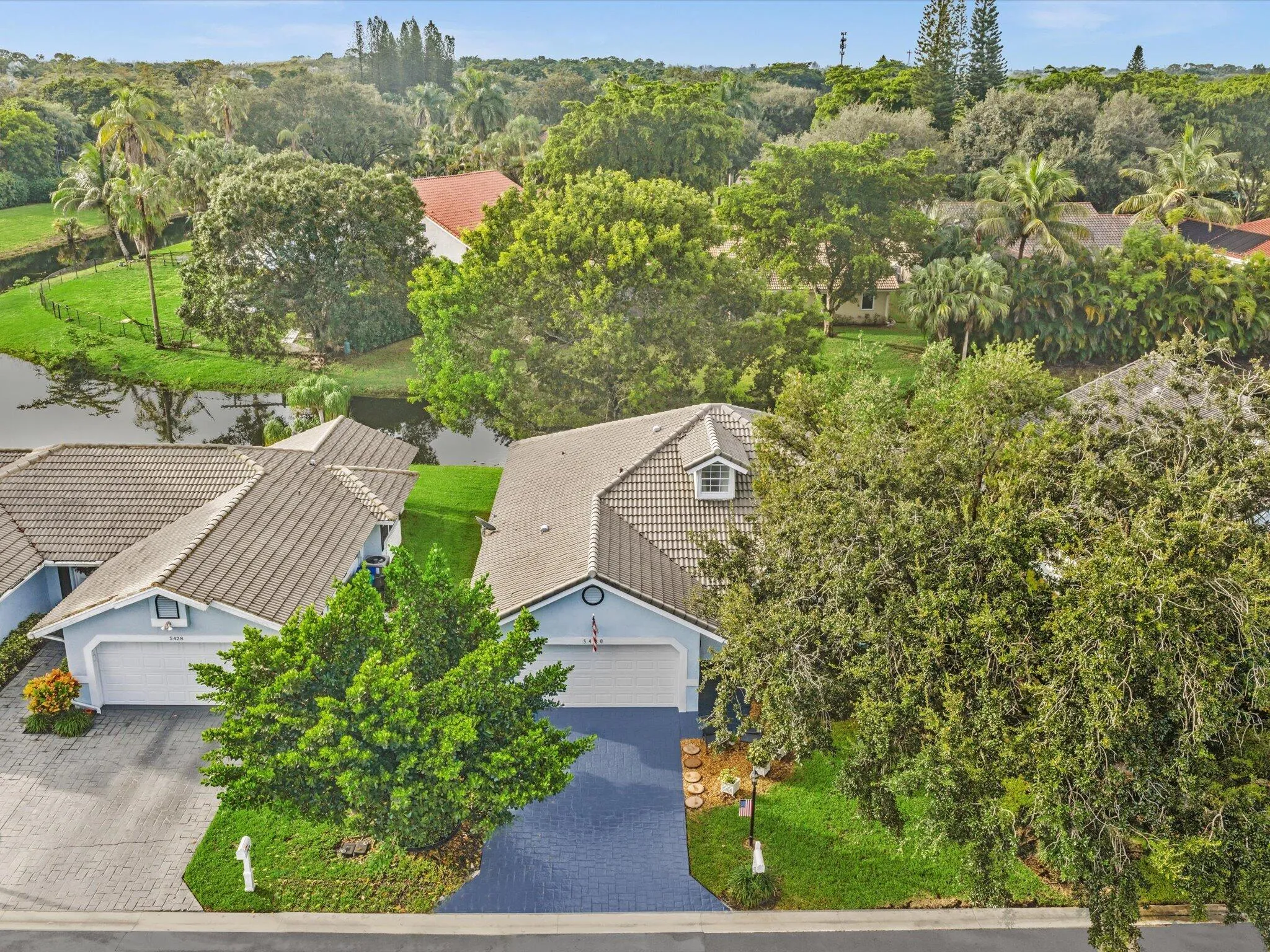 Paved driveway, tile roof, dormer window, mature trees, and landscaped grounds