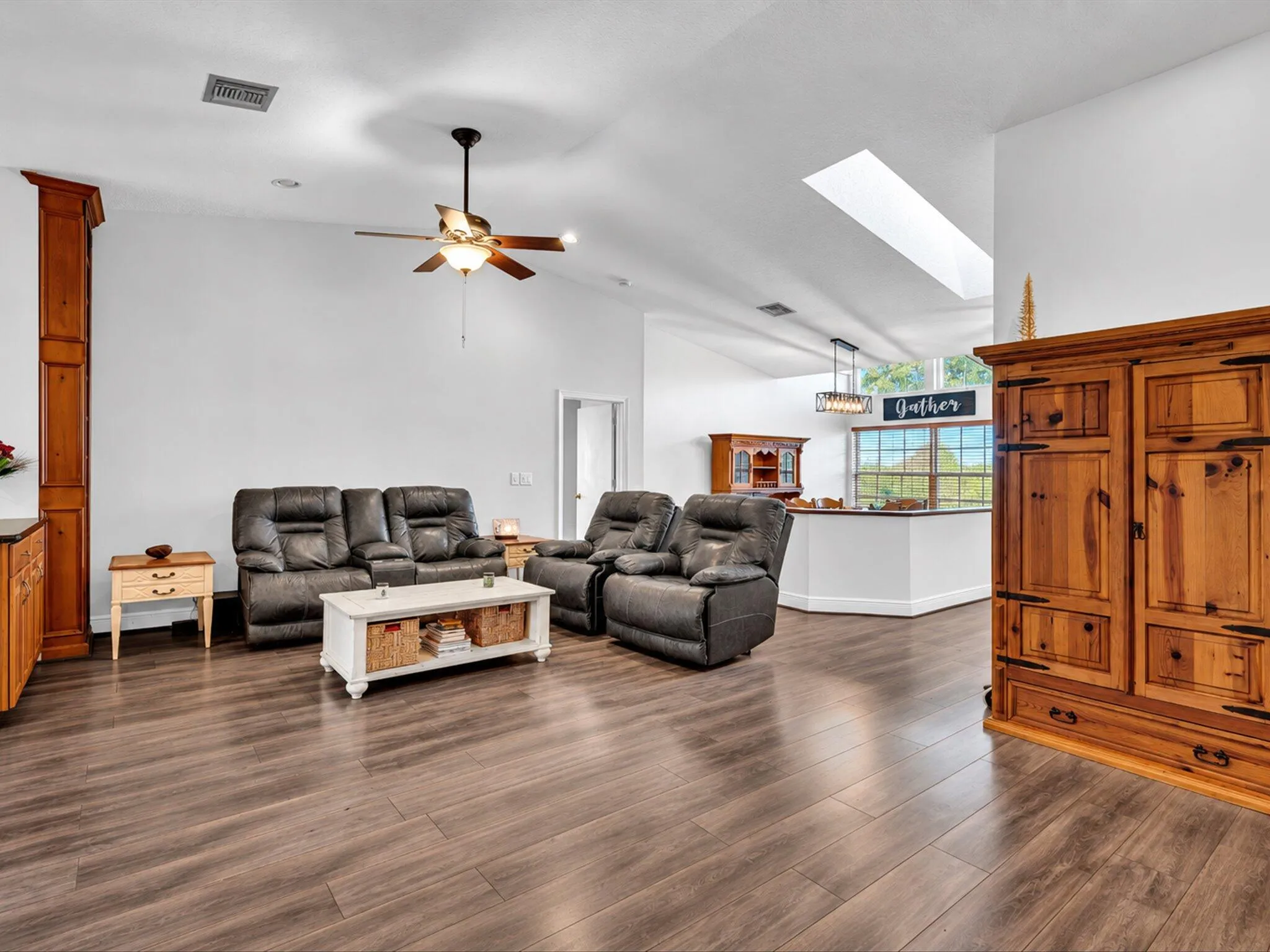 Vaulted ceiling with skylight, wood-finish flooring, ceiling fan, and architectural column