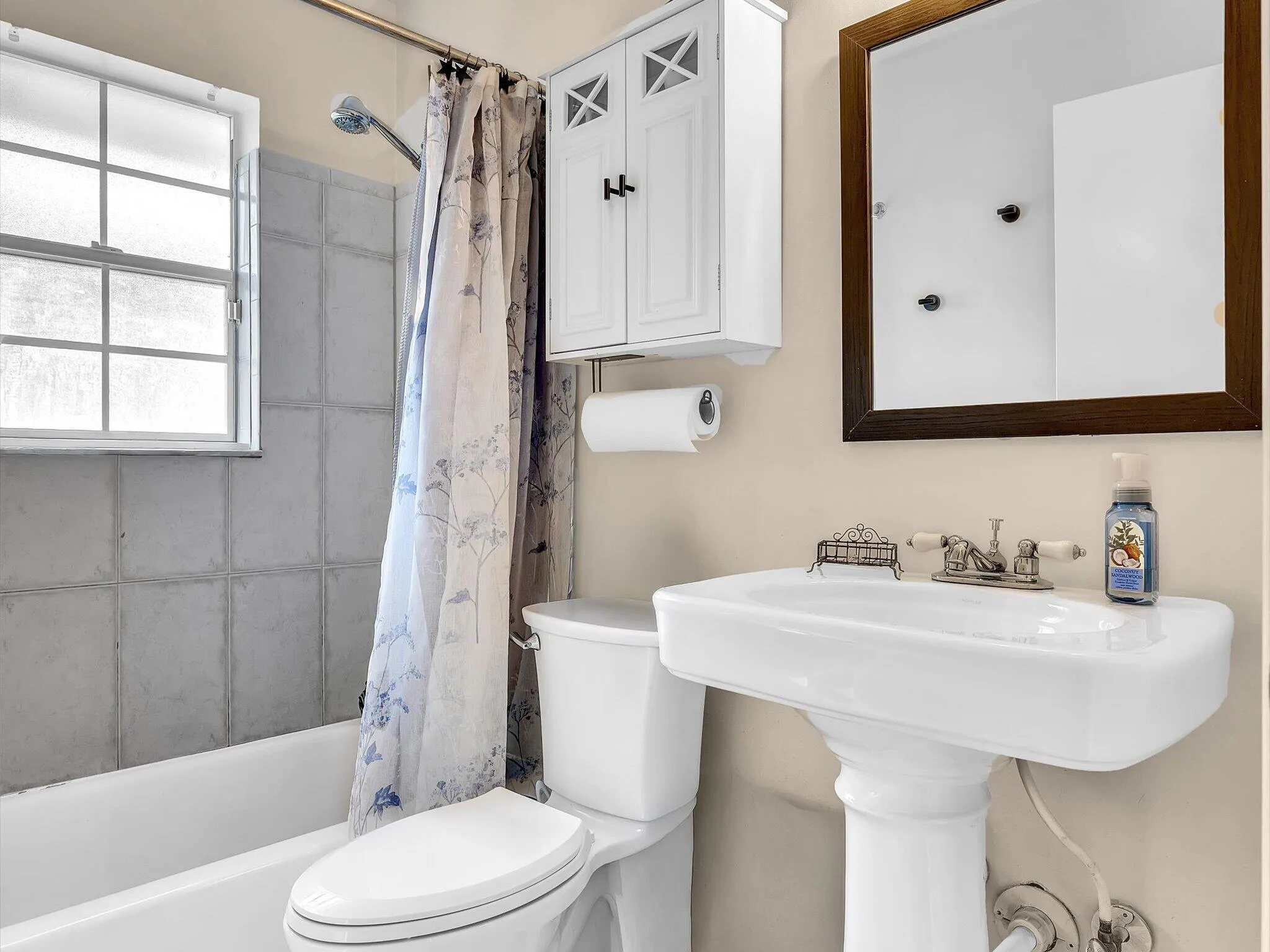 Pedestal sink with dual-handle faucet, framed mirror, and wall-mounted storage cabinet