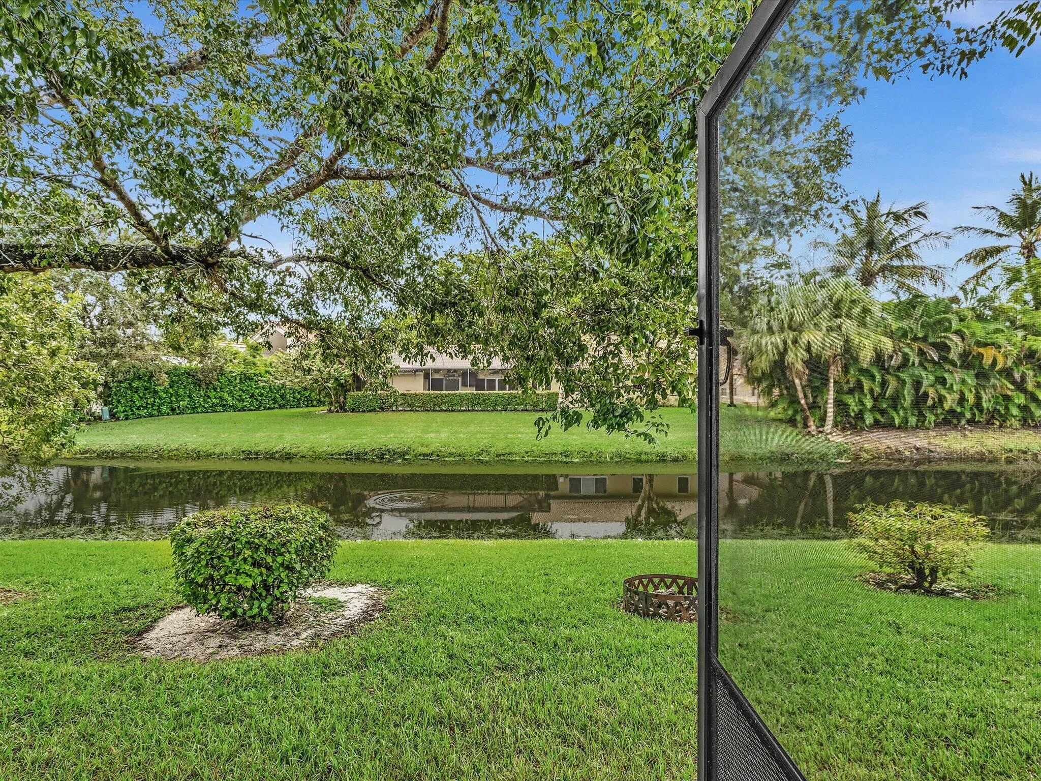 Expansive green lawn with established trees and manicured shrubbery, bordering a water feature