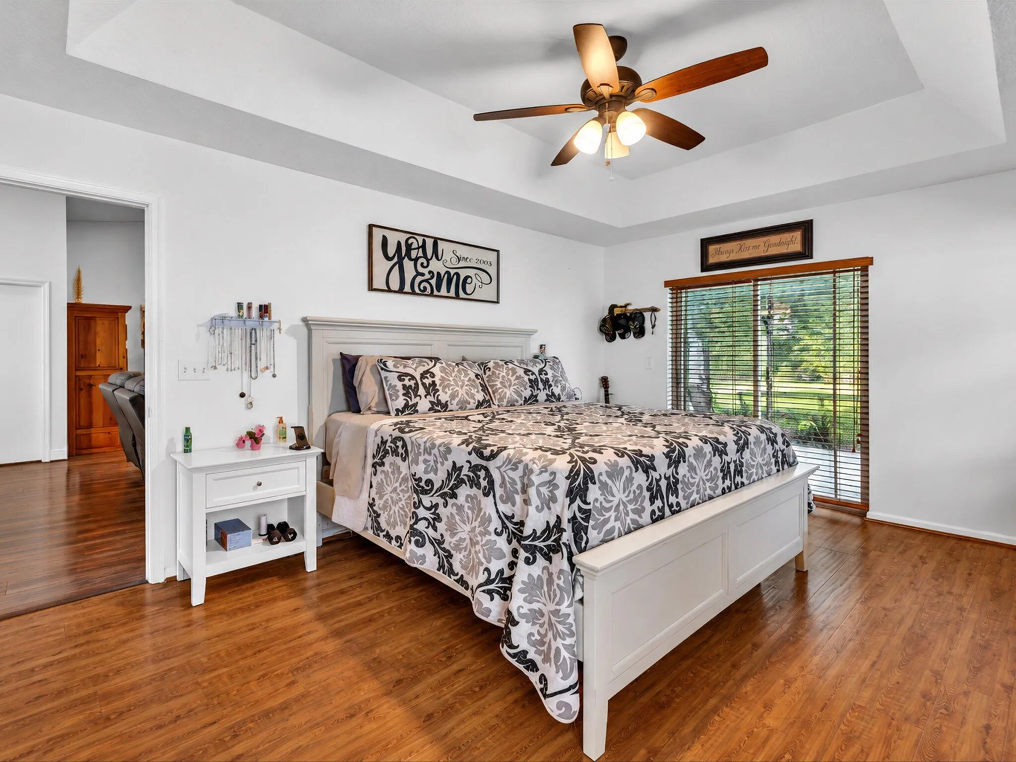 Tray ceiling with a ceiling fan, wood-finish flooring, and a sliding glass door with horizontal blinds