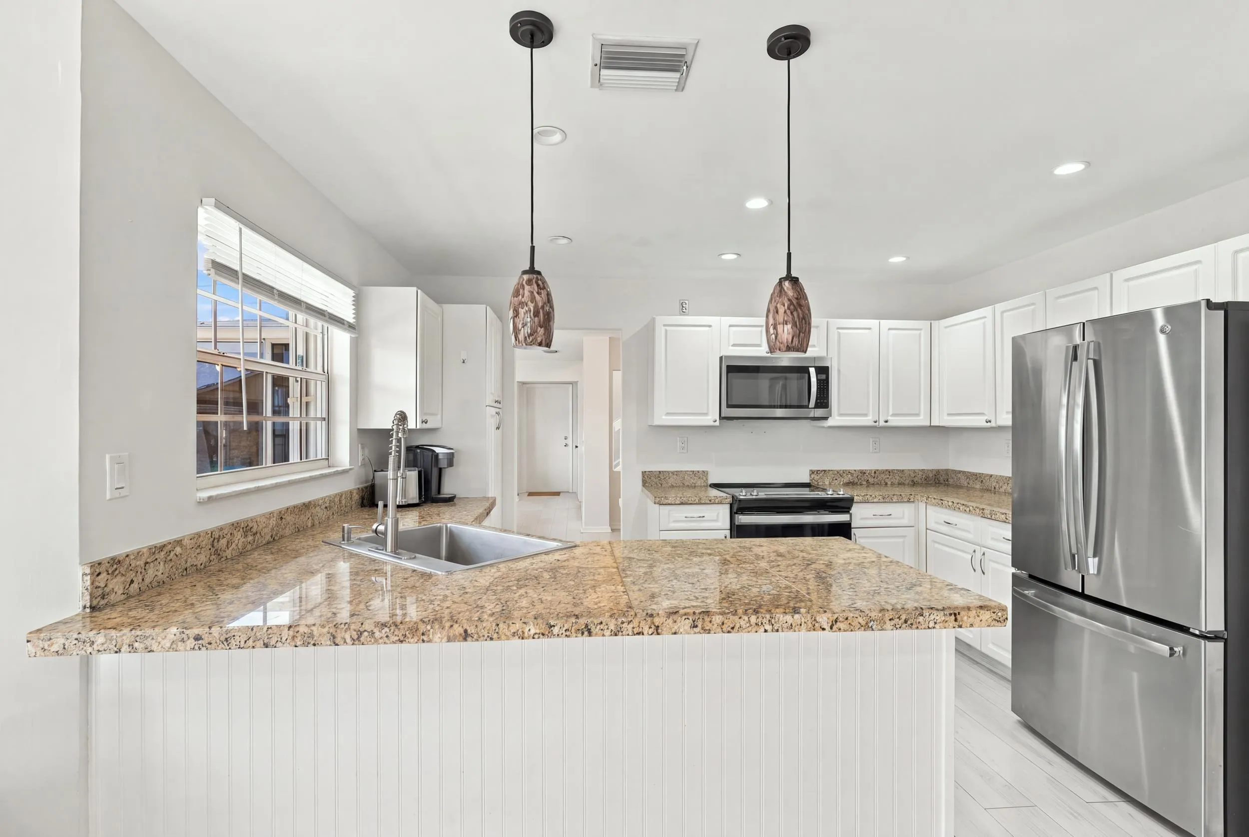 The bright eat-in kitchen features contemporary white cabinetry, granite countertops, new stainless steel appliances, and a convenient breakfast bar. Abundant natural light, space for casual dining, and sliding glass doors create a seamless connection to the private backyard.