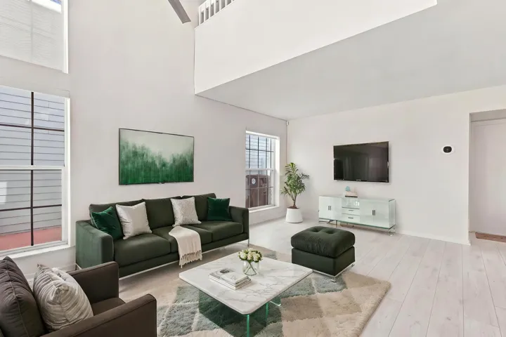 Soaring 15-foot ceilings and expansive windows fill the living room with natural light, creating a warm and welcoming space for everyday living and entertaining. The thoughtfully designed floor plan flows effortlessly from the living area to a convenient powder room and the private backyard, making the home feel open, connected, and inviting.