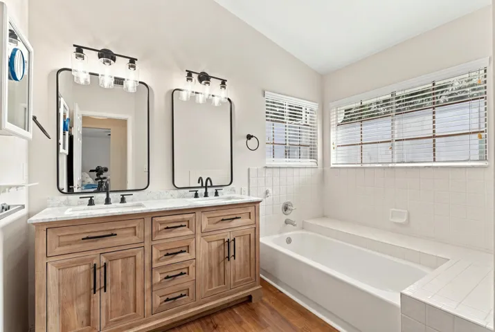 The fully updated primary ensuite exudes refined elegance with a natural oak vanity, quartz countertops, new fixtures, a relaxing bathtub, and a beautifully finished shower with a frameless glass enclosure.