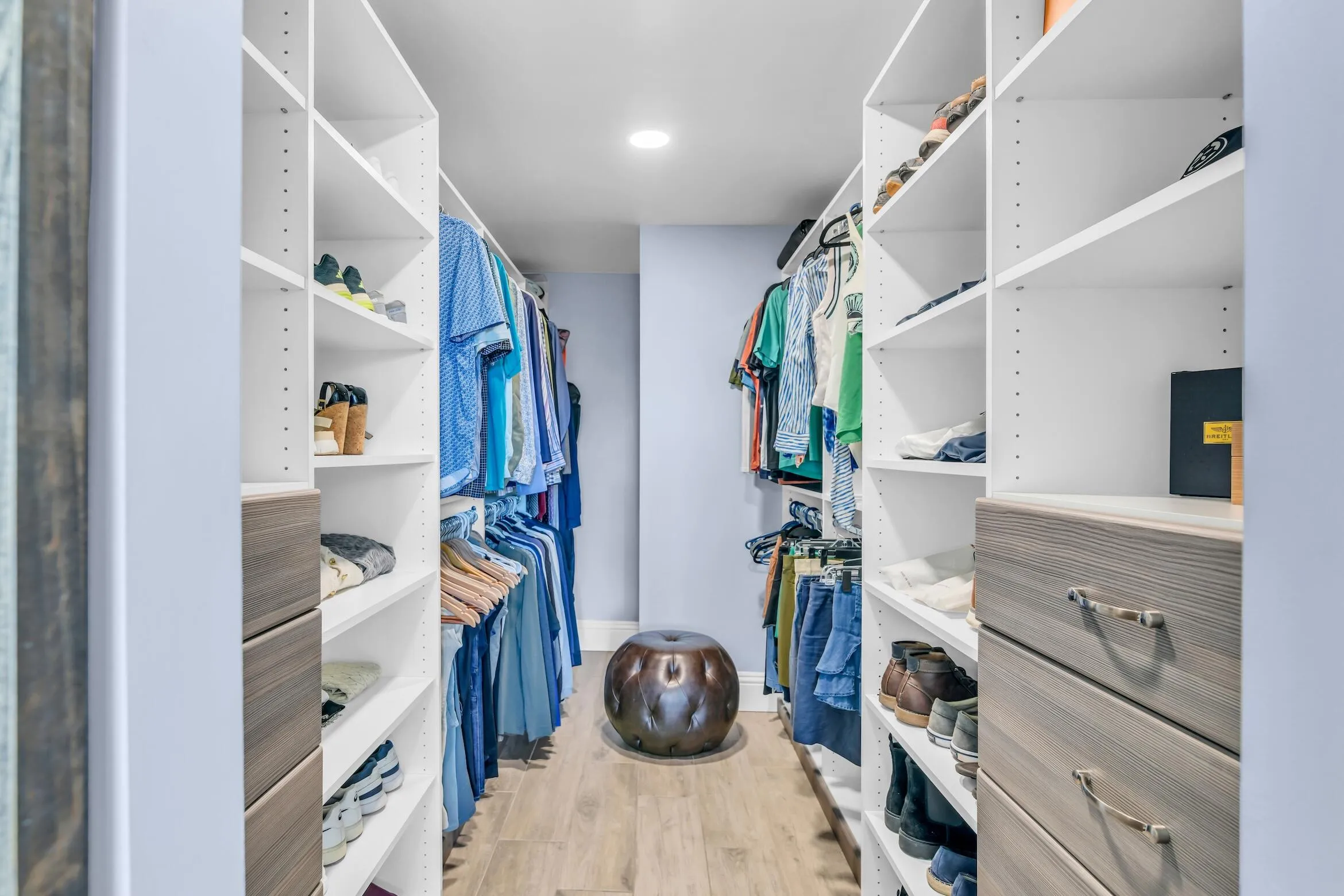 Large walk-in primary bedroom closet has custom wood look built-ins complementing the cabinets in the bathroom.