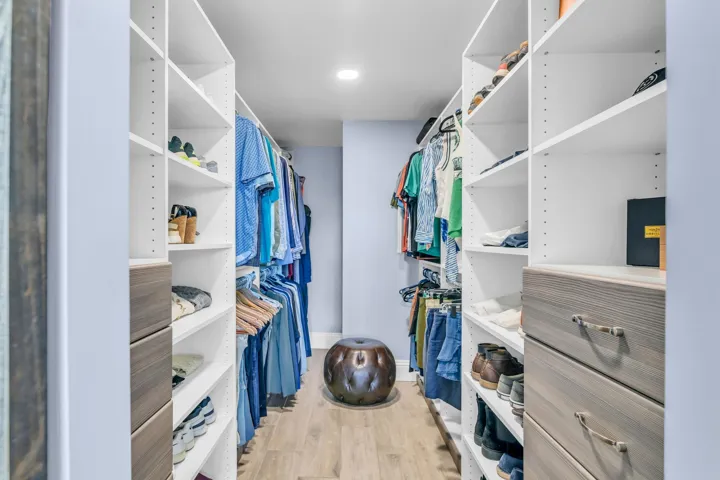 Large walk-in primary bedroom closet has custom wood look built-ins complementing the cabinets in the bathroom.