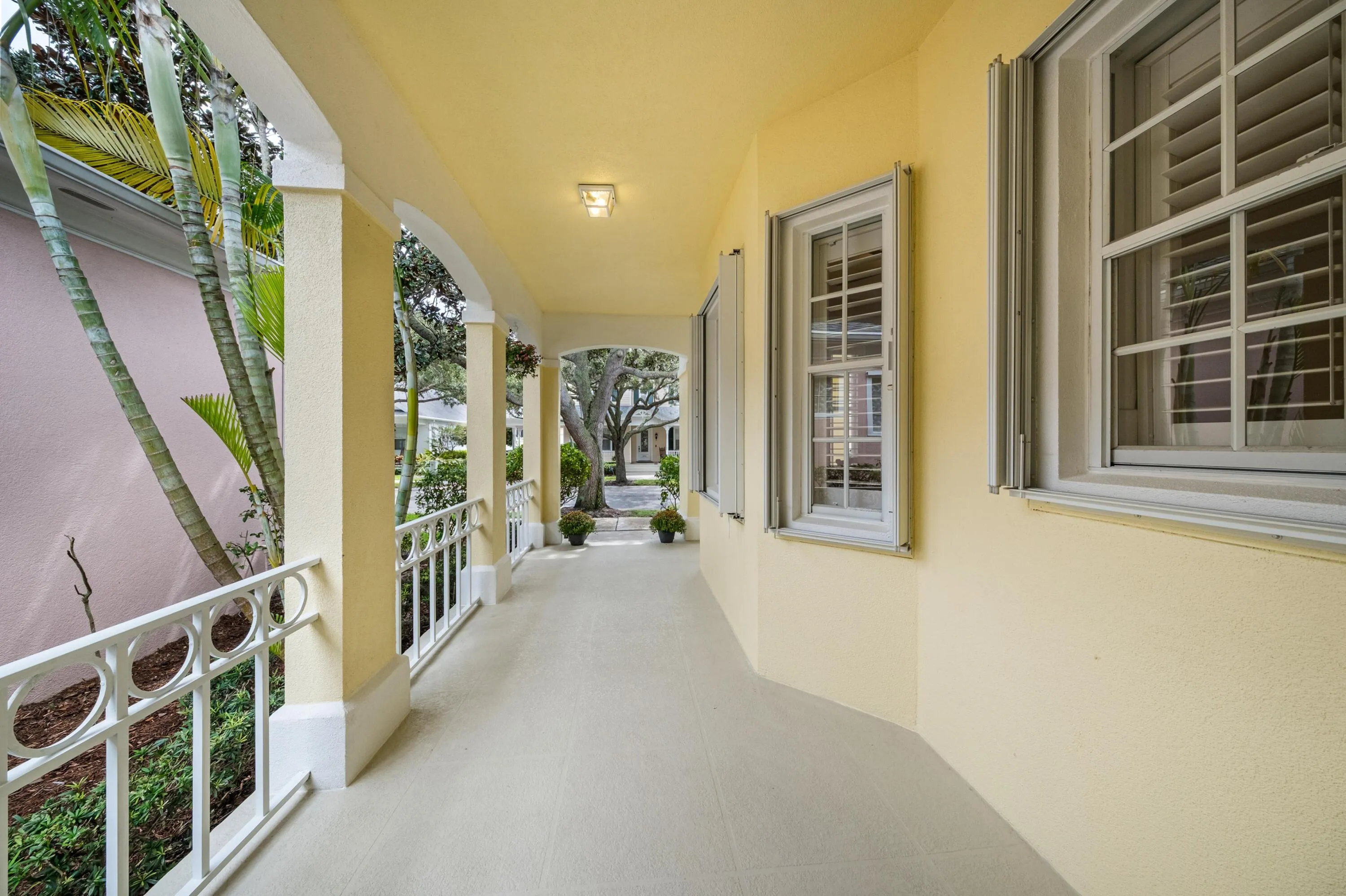Covered front porch colonnade with decorative railings, framing views of the mature oaks