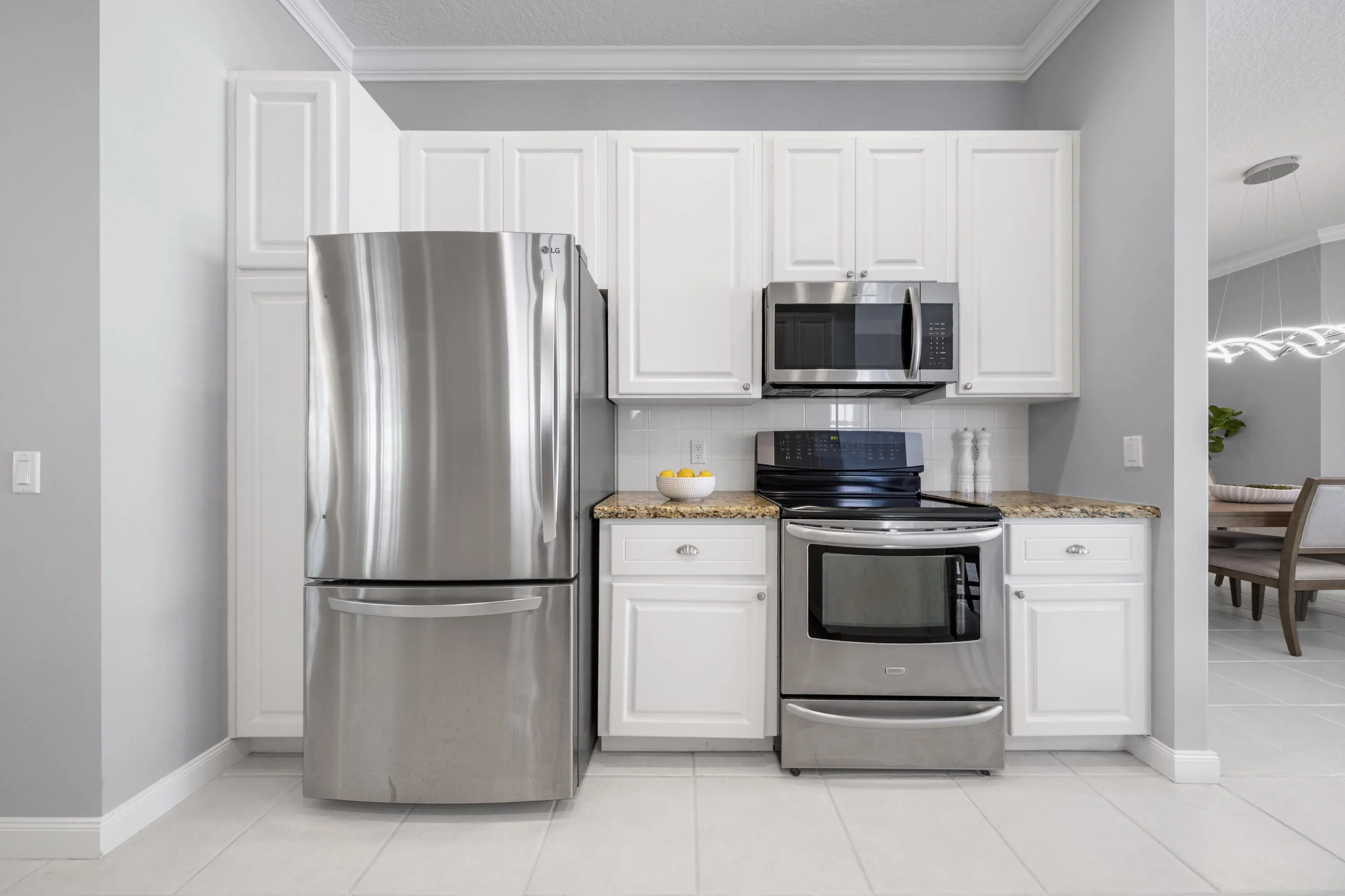 Newer stainless refrigerator, range and microwave framed by white cabinetry and granite