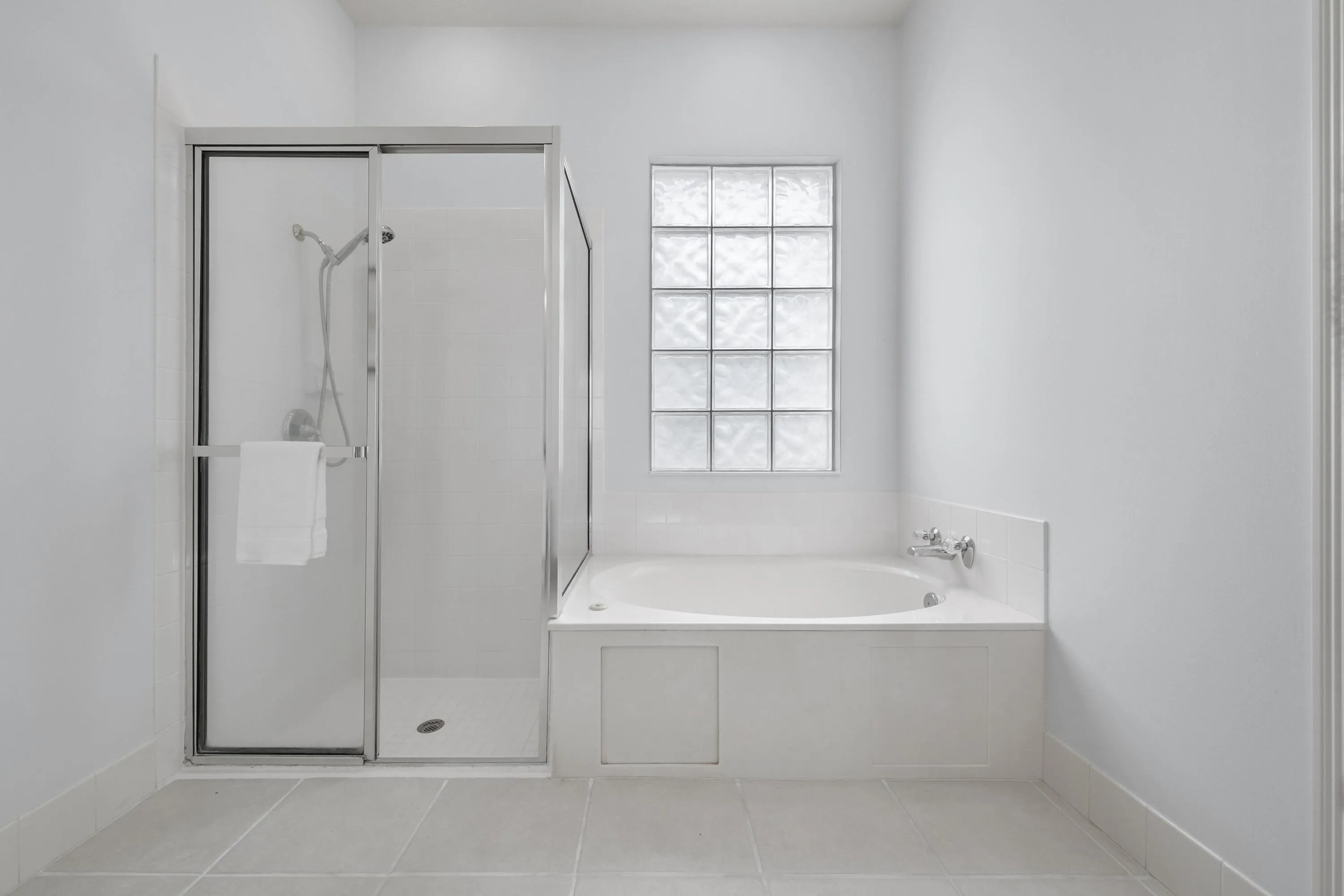 Primary bathroom with walk-in shower and soaking tub beneath a glass block window