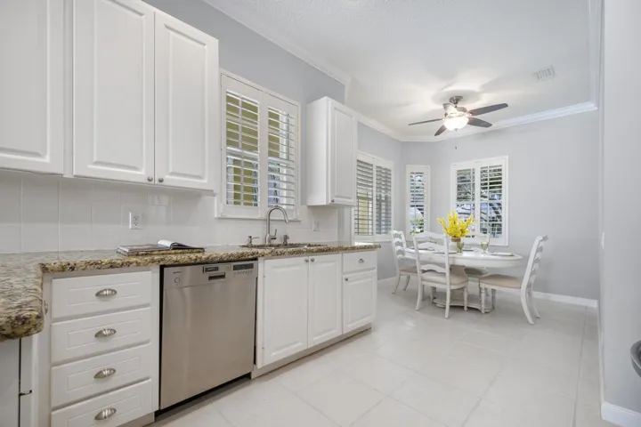 Double sink beneath plantation shutters, beside a window-lined breakfast nook with plenty of natural light