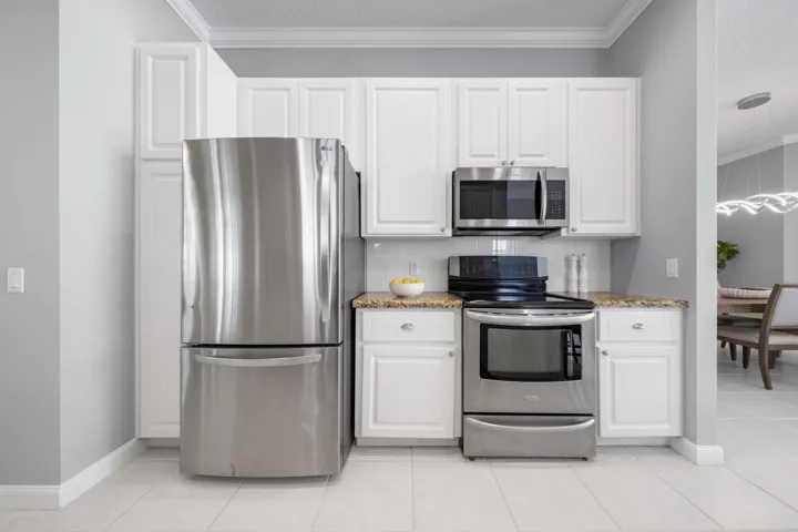 Newer stainless refrigerator, range and microwave framed by white cabinetry and granite