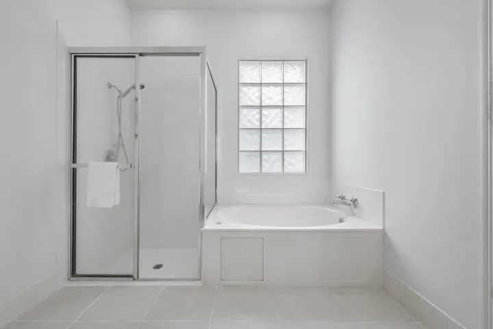 Primary bathroom with walk-in shower and soaking tub beneath a glass block window