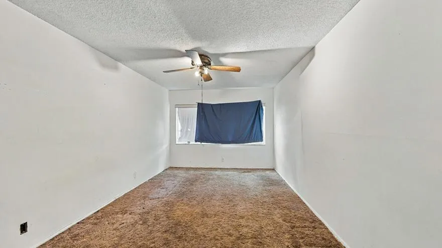 Window with partial covering, ceiling fan with integrated lighting, textured ceiling, light-toned walls, and carpet flooring