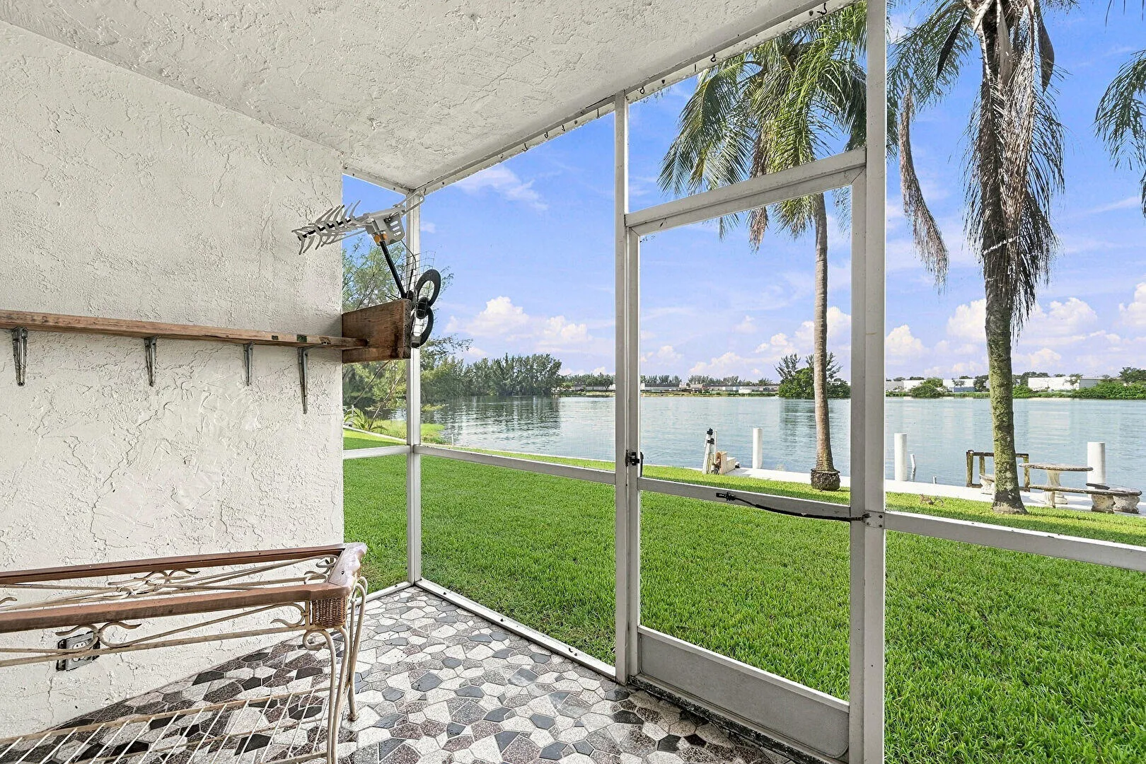 Screened patio with patterned tile flooring, offering direct access to a manicured lawn and waterfront