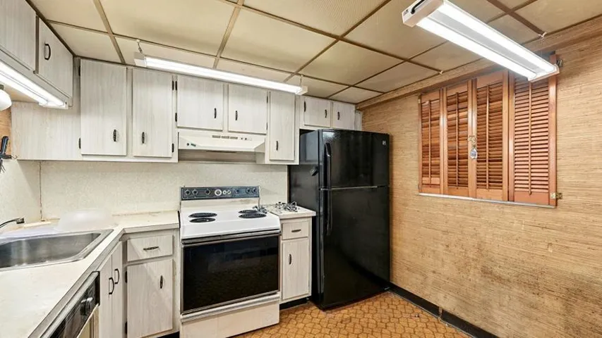 Kitchen featuring white cabinetry with dark hardware, a stainless steel sink, a white electric range, and a black refrigerator