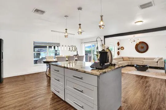 Kitchen island with stone countertop, wood-finish flooring, and pendant lighting