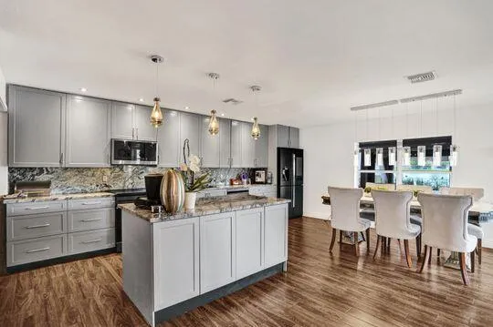 Modern kitchen featuring gray cabinetry, stone countertops, a central island, stainless steel appliances, and wood-finish flooring