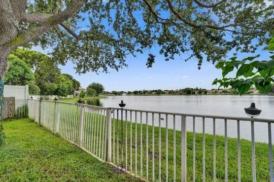 Expansive waterfront property featuring a white metal fence, lush green lawn, and mature trees