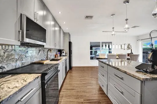 Kitchen featuring wood-finish flooring, granite countertops, full-height granite backsplash, a kitchen island with storage, and pendant lighting fixtures