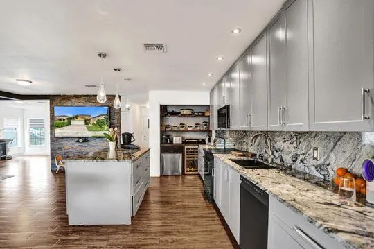 Wood-finish flooring throughout, complemented by a kitchen island with pendant lighting, gray cabinetry, and stone countertops with a matching backsplash