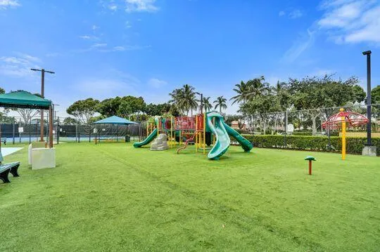 Playground with artificial turf surfacing, multiple slides, climbing structures, and shaded seating areas