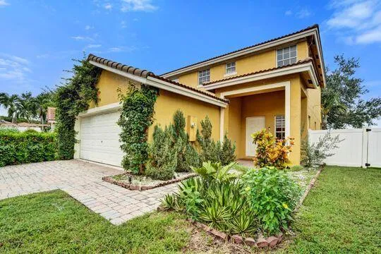 Stucco exterior with a tiled roof, paver driveway, an attached garage, and a white fence