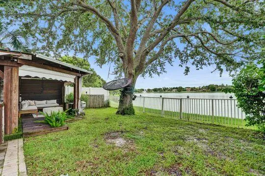 Expansive backyard with a manicured lawn, established mature tree, and a built-in wood-frame gazebo with a retractable awning