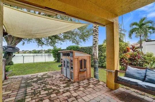 Brick paver patio with a fabric shade structure and a porch swing, overlooking a manicured lawn and water