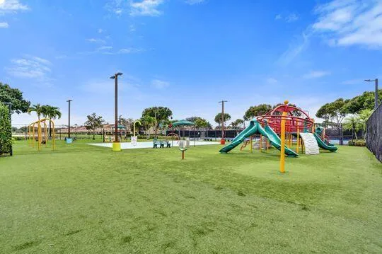 Expansive recreational area featuring artificial turf, a colorful playground structure with slides, swings, and a splash pad