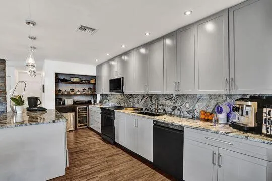 Galley kitchen featuring gray cabinetry, granite countertops, a full-height stone backsplash, recessed lighting, and wood-finish flooring