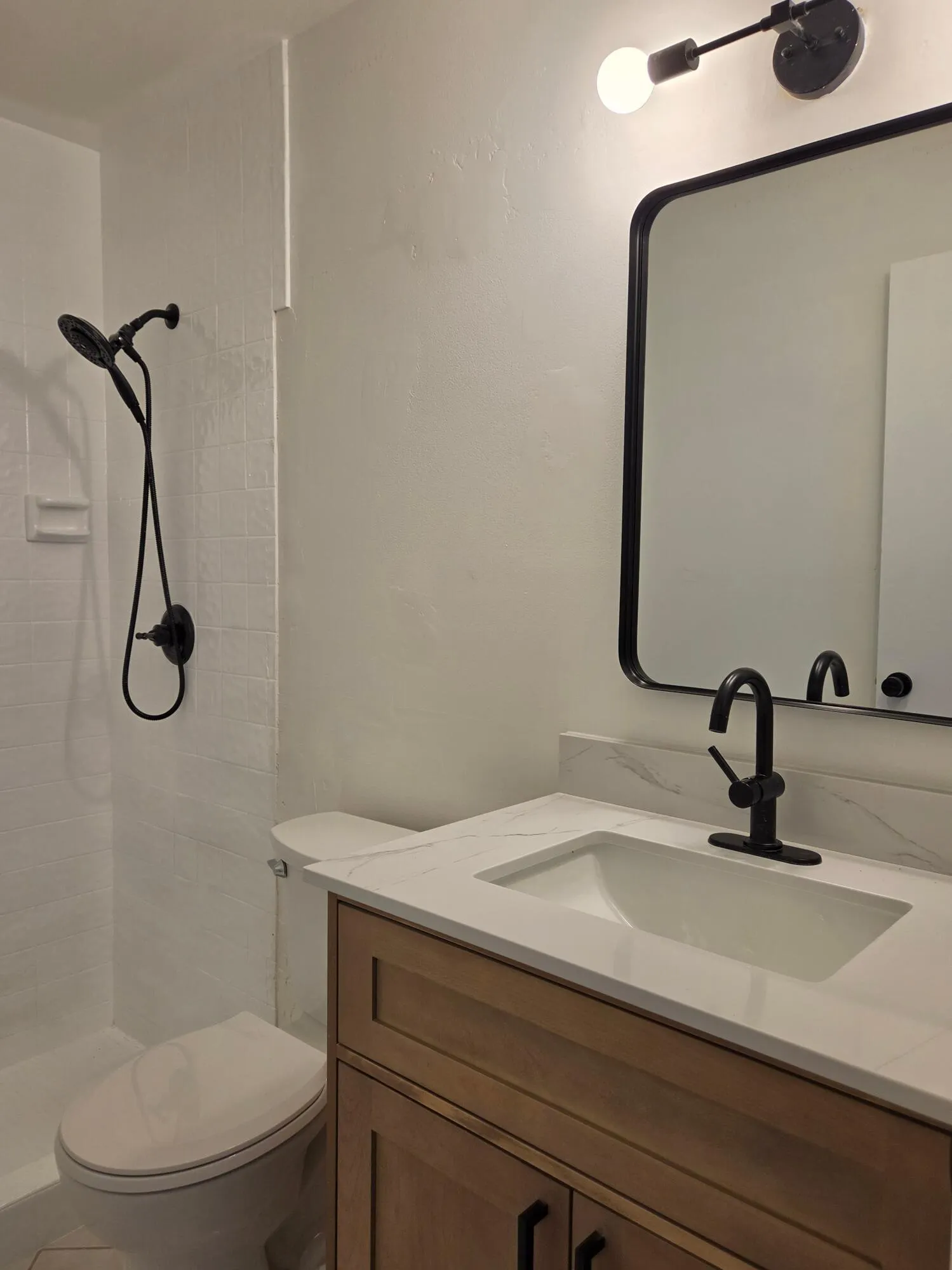 Bathroom featuring a wood-finish vanity with an integrated sink, a dark-framed mirror, and a matte black faucet