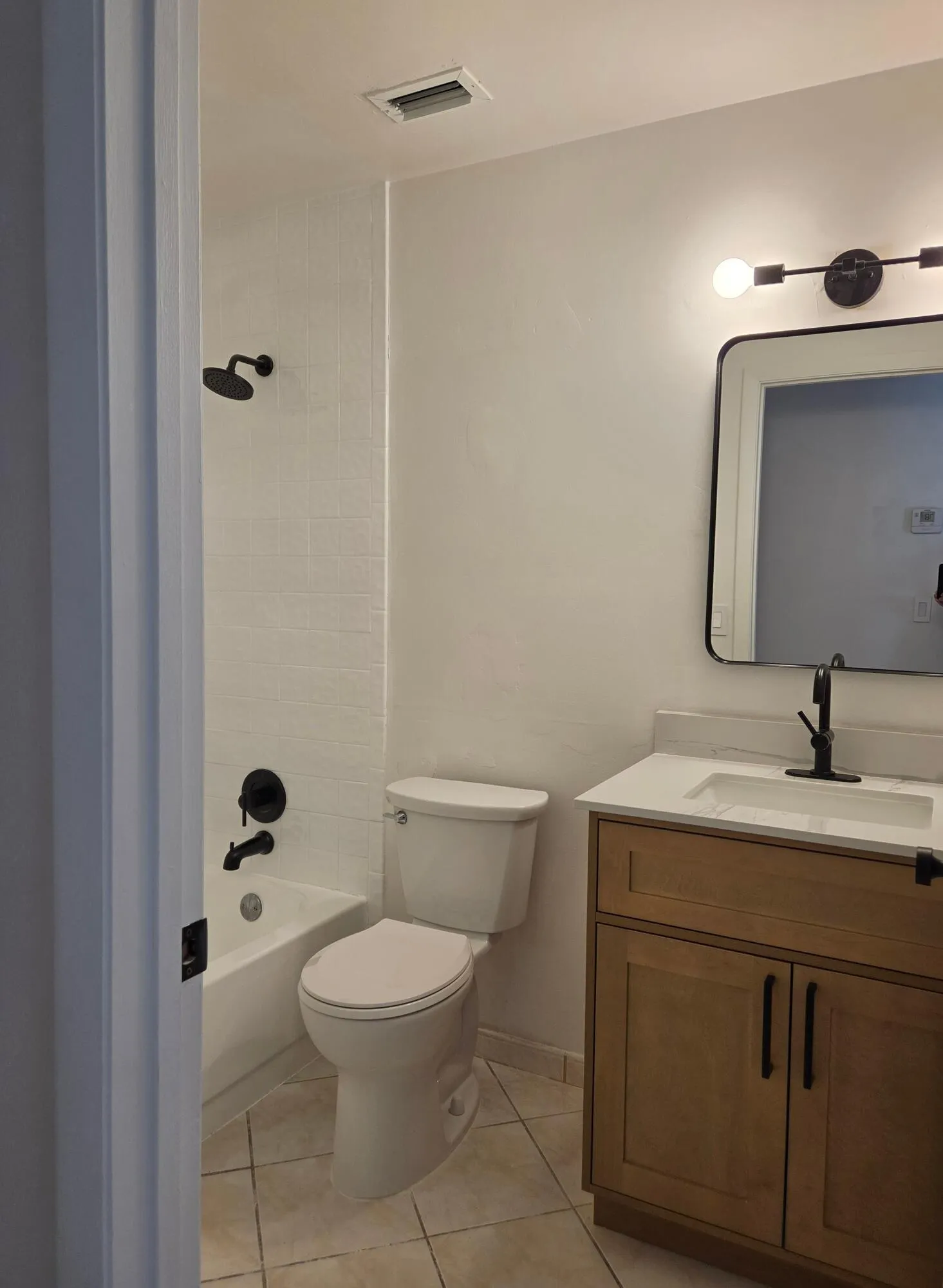 Bathroom featuring a single vanity with stone countertop, matte black fixtures, tile flooring, and a shower-tub combination with subway tile surround