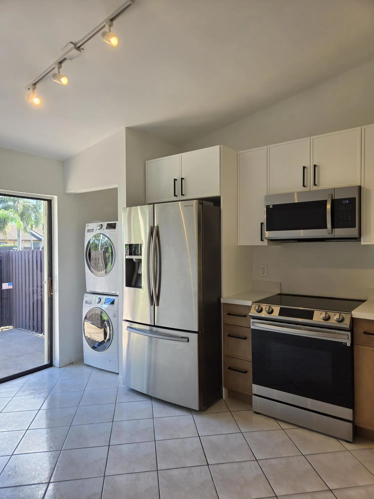Stainless steel appliances, track lighting, white upper cabinetry, wood-finish lower cabinetry, and tiled flooring