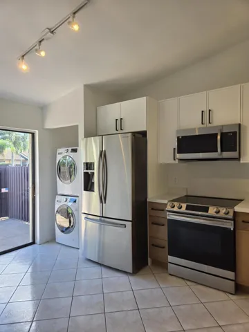 Stainless steel appliances, track lighting, white upper cabinetry, wood-finish lower cabinetry, and tiled flooring