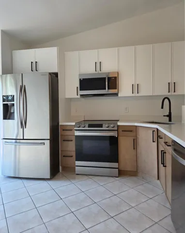 Stainless steel appliance suite, white upper cabinetry, wood-finish lower cabinetry, light-toned countertops, and tiled​​‌​​​​‌​​‌‌​‌‌​​​‌‌​‌​‌​‌​​​‌​​ flooring