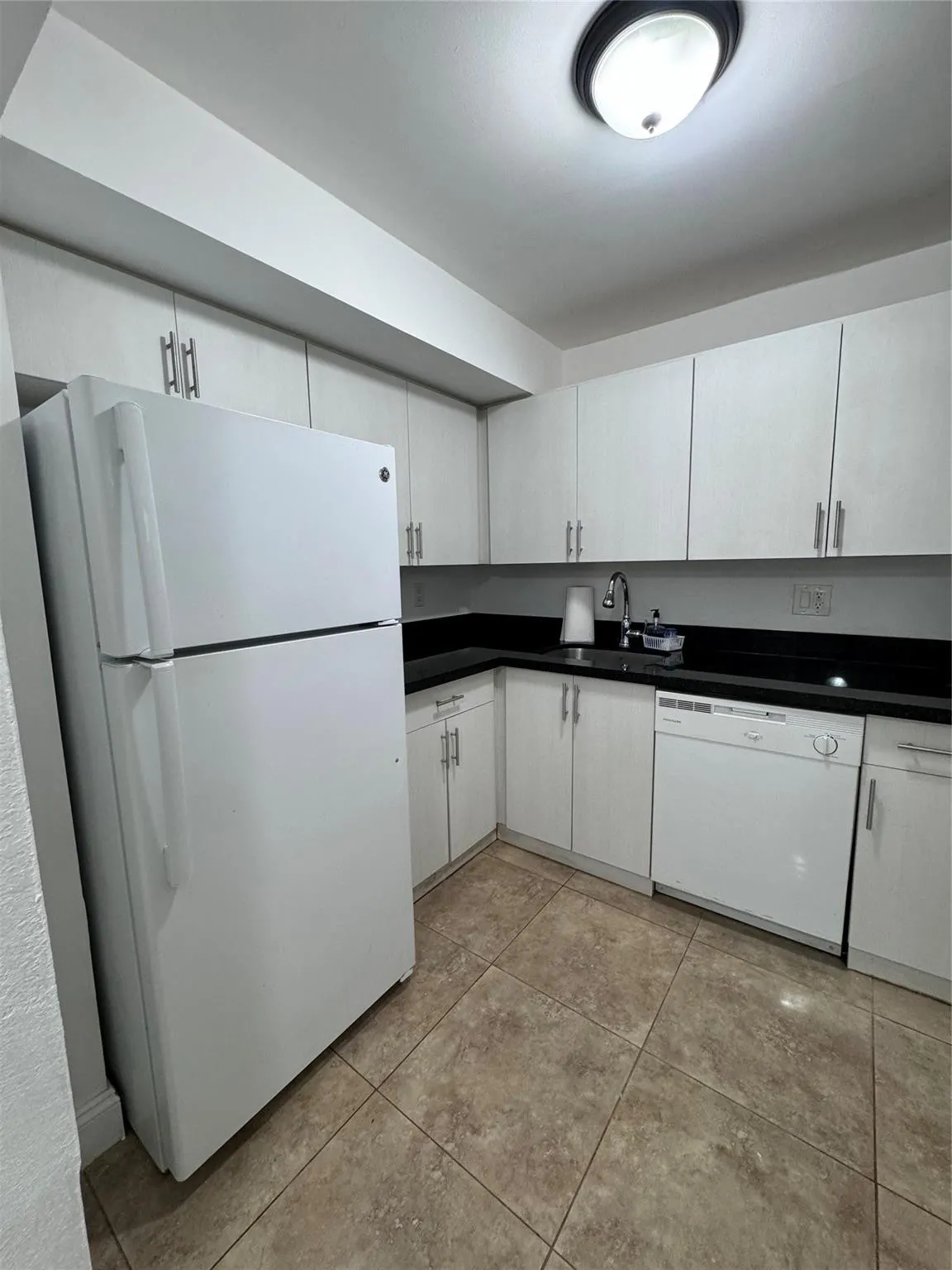 Kitchen featuring white cabinetry, dark countertops, a white refrigerator, a white dishwasher, and tile flooring